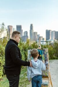 a man standing beside a child drawing on a wooden easel